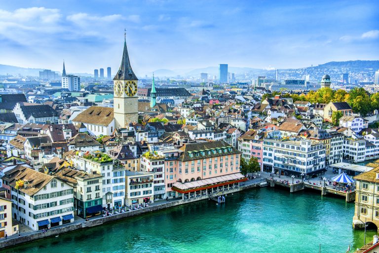 Aerial view of Zurich, Switzerland. Taken from a church tower overlooking the Limmat River. Beautiful blue sky with dramatic cloudscape over the city. Visible are many traditional Swiss houses, bridges and churches.